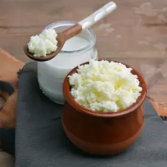 Grani di latte di kefir in un vasetto di terracotta e su un cucchiaio di legno, accanto a un bicchiere di latte di kefir.