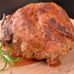 Soczysta szynka pieczona na obiad, aromatyczna i przyprawiona, podana z gałązką rozmarynu na drewnianej desce.