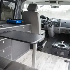 Wnętrze kampera z kuchenką turystyczną i rozkładanym stolikiem. Idealne auto na kampera dla podróżników.