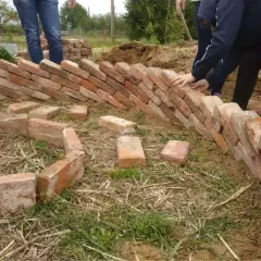 Costruzione di un keyhole garden con mattoni. Mani che posizionano i mattoni per creare la forma circolare.