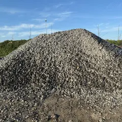Duża hałda szarego żwiru na tle błękitnego nieba z chmurami.