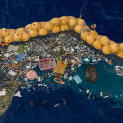 Sieć rybacka z żółtymi bojami zbiera dryfujące śmieci na oceanie, w tym plastik i oponę.
