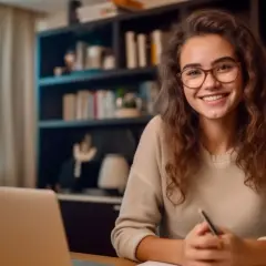 Lächelnde junge Frau mit Brille lernt am Laptop. Sie nutzt die Zeit für ein Bildungsurlaub Fernstudium, um sich weiterzubilden.