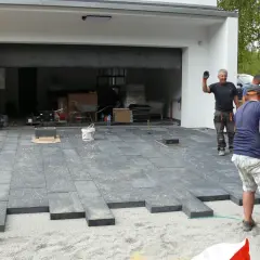 Budowa podjazdu z kostki brukowej, mężczyźni układają płyty betonowe.