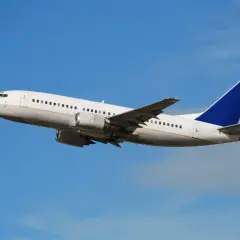 Biały samolot pasażerski z niebieskim ogonem, jeden z najpopularniejszych samolotów pasażerskich, wznosi się na tle błękitnego nieba.