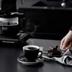 En kopp ångande kaffe från Moccamaster, perfekt för en stunds njutning. Visste du att kaffe nyttigt kan vara? Mörk choklad bredvid.