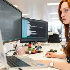 Rudowłosa programistka pracuje przy komputerze, monitor wyświetla kod. Czas na aktualizację sterowników.