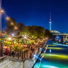 Serata vivace in un club all'aperto a Berlino, con luci colorate, gente che balla e la Torre della Televisione sullo sfondo.