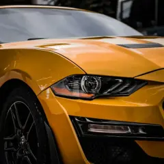 Żółty Ford Mustang z błyszczącym lakierem, jakby był pomalowany farbą akrylową, z detalami reflektorów i grillem.