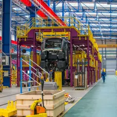 W hali produkcyjnej Alstom Konstal powstaje nowoczesny pociąg. Widać fragmenty konstrukcji, podnośniki i pracownika w niebieskim kombinezonie.