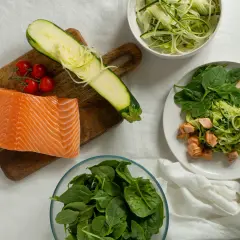 Składniki na dietę low carb przepisy: surowy łosoś, cukinia spiralizowana, pomidorki koktajlowe i świeży szpinak.