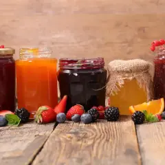 Słoiki z dżemami i miodem, otoczone świeżymi owocami. Pektyna co to? Naturalny zagęstnik do domowych przetworów.