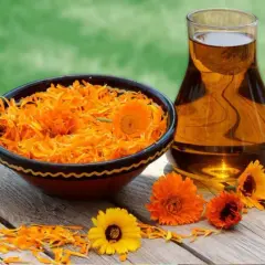 Petali di calendula in una ciotola e olio dorato in un bicchiere, rimedi naturali per il prurito.