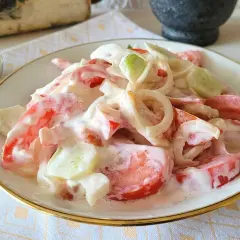 Pyszna sałatka pomidor ogórek cebula w kremowym sosie, podana na talerzu z ozdobną łyżką.