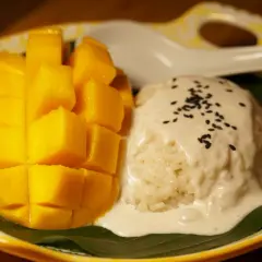 Ein Teller mit süßem Mango Sticky Rice, garniert mit Kokosmilch und Sesam. Ein köstlicher Nachtisch!