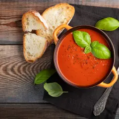 Aksamitny zupa krem z pomidorów, udekorowana bazylią, podana z chrupiącym pieczywem i łyżką.