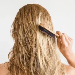 Kobieta szczotkuje mokre, blond włosy. Może to być część rytuału pielęgnacyjnego z użyciem imbiru na włosy.