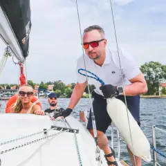Mężczyzna z uprawnieniami żeglarza jachtowego steruje jachtem, podczas gdy jego załoga cieszy się rejsem.