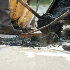 Robotnicy rozkładają gorący asfalt za pomocą łopat i walca.