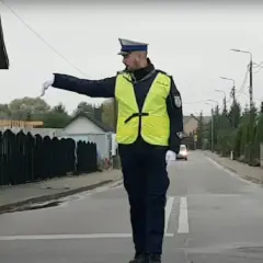 Policjant w kamizelce odblaskowej kieruje ruchem na ulicy, wskazując ręką kierunek.