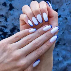 Elegancki **manicure francuski** z białymi paznokciami i niebieskimi końcówkami na tle granatowego materiału.