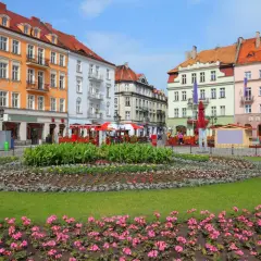 Kolorowy rynek w najstarszym mieście w Polsce, z kwitnącymi rabatami kwiatowymi i kolorowymi kamienicami w tle.