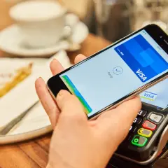 Bezahlvorgang mit Apple Pay: Ein Smartphone hält über einem Kartenlesegerät, daneben ein Stück Kuchen.