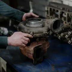 Mechanik trzyma gruszkę turbiny, przygotowując ją do montażu. Obok leży blok silnika.