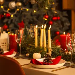 Uroczysta wigilia w restauracji: pięknie nakryty stół z czerwonymi świecami, szyszkami i choinką w tle.