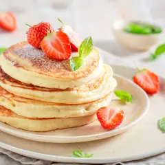 Pancake con yogurt e fragole fresche, spolverati di zucchero a velo e decorati con foglie di menta.