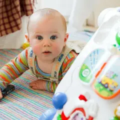 Bobas w 6 miesiącu życia, w kolorowym ubranku, leży na macie obok zabawki edukacyjnej. To jego skok rozwojowy!