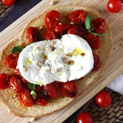 Pyszna bruschetta z burratą, pieczonymi pomidorkami koktajlowymi i orzeszkami pinii. Idealna na lekki posiłek.