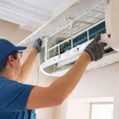 Fachowiec w niebieskiej czapce i rękawiczkach montuje klimatyzację w domu, dbając o każdy szczegół instalacji.