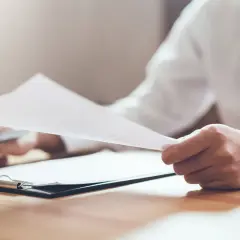 Mężczyzna w białej koszuli i czarnym krawacie przegląda dokumenty. Może to być związane ze zgłoszeniem najmu okazjonalnego po terminie.