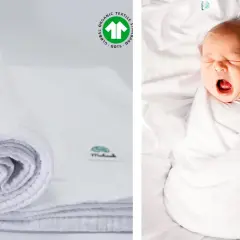 Biały, zwinięty otulacz muślinowy obok śpiącego niemowlaka. Certyfikat GOTS potwierdza jego ekologiczne pochodzenie.