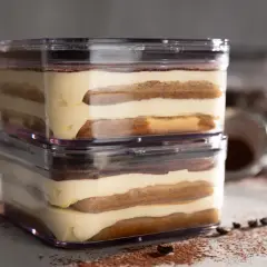 Zwei Schichten sally tiramisu im transparenten Behälter, mit Kakaopulver und Kaffeebohnen bestreut.