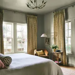 A cozy bedroom with a bed, a chair, and a floor lamp. The curtains are a beautiful millenial green, adding a touch of nature to the room.