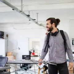Junger Mann mit Fahrrad und Rucksack im Büro, bereit für sein online studium in Berlin.