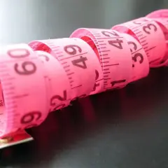 Różowa miarka krawiecka zwinięta w spirale, z widocznymi centymetrami. Idealna do określenia rozmiaru buta 2 latka.