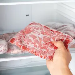 Ręka wyjmuje z zamrażarki paczkę mrożonego mięsa.