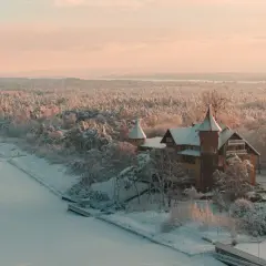 Zimowy krajobraz Łeby: pokryty śniegiem las, zamarznięte jezioro i zabytkowy budynek z wieżyczkami.
