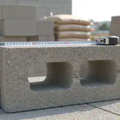 Un parpaing est mesuré avec un mètre ruban. La dimension du parpaing est visible sur l'outil.