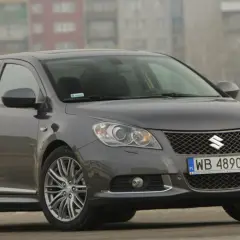 Szary Suzuki Kizashi z felgami i tablicą rejestracyjną WB 4890E na tle budynków.