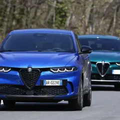 Dwa Alfa Romeo Tonale, jeden niebieski z przodu, drugi zielony z tyłu, jadą drogą. Sprawdź alfa romeo tonale cena.