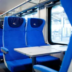 Wygodne, niebieskie siedzenia w przedziale konduktorskim PKP Intercity. Stoliki gotowe na podróż.