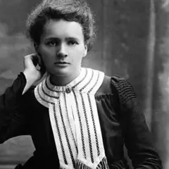 Czarno-białe zdjęcie Marii Skłodowskiej-Curie w eleganckiej sukni z ozdobnym kołnierzem.