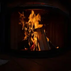 Flammen lodern im Kaminofen. Ein Zeitungsstapel liegt davor. Der Ofen ist nicht stillgelegt, es gibt Ausnahmen für gemütliche Abende.