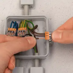 Mains électriques connectées dans une boîte encastrée. Le diamètre de la boîte encastrement permet d'accueillir les fils et les connecteurs.