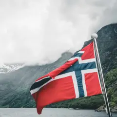 Norweska flaga na tle fiordu i gór. Marzysz o pracy w Norwegii? Sprawdź najlepiej płatne zawody w Norwegii!