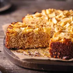 Ein saftiger Haferflocken Kuchen mit Apfelstücken, auf einem Holzbrett, bereit zum Genießen.